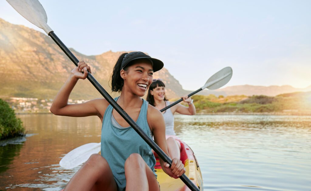 Two smiling friends kayaking on a lake together during summer break. Smiling and happy playful women bonding outside in nature with water activity. Having fun on a kayak during weekend recreation