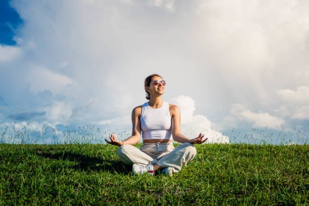 Young woman dressed in white and sitting in the green meadow on a blue sky day.