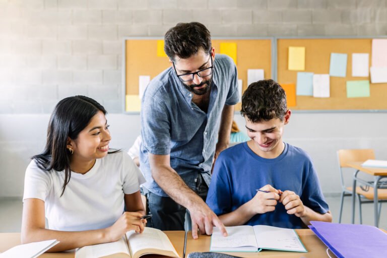 Male teacher helping high school students doing exercises in classroom