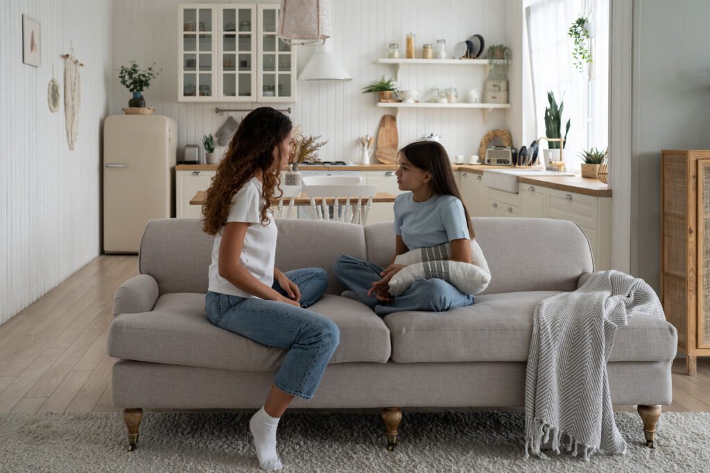Serious mother and teenage girl are both sits on sofa in apartment discussing important topics