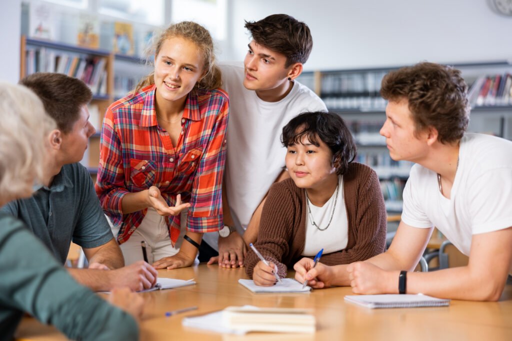 Positive teenage students working and discussing in groups in library