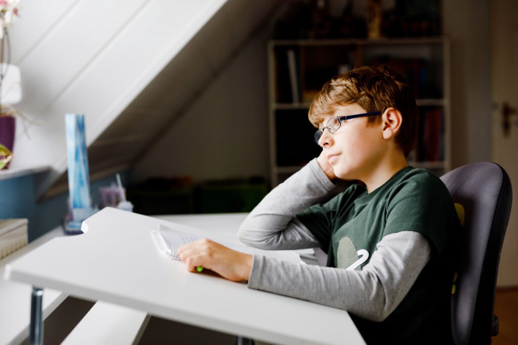 Kid boy with glasses learns at home for school. Preteen child making homework. Home schooling and distance learning concept.