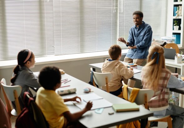 Smiling African American Teacher Talking to Children in Classroom at Primary School