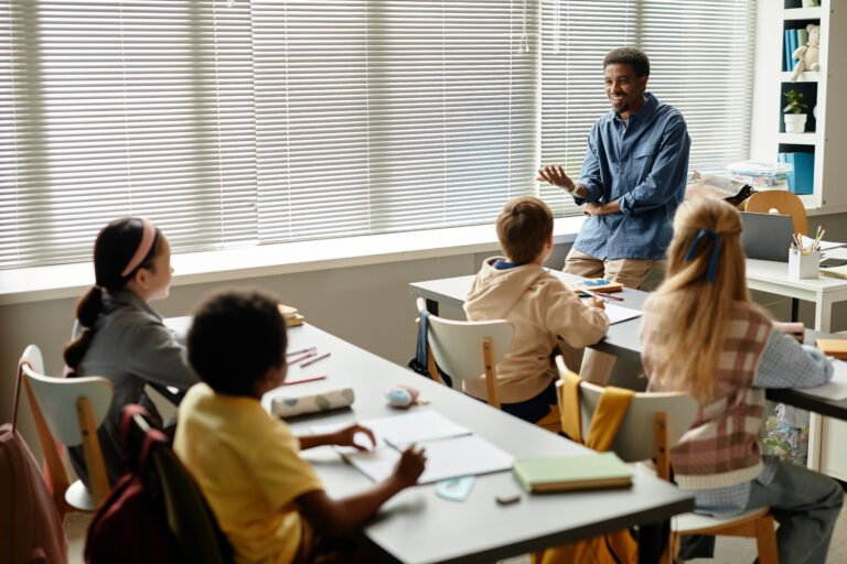 Smiling African American Teacher Talking to Children in Classroom at Primary School