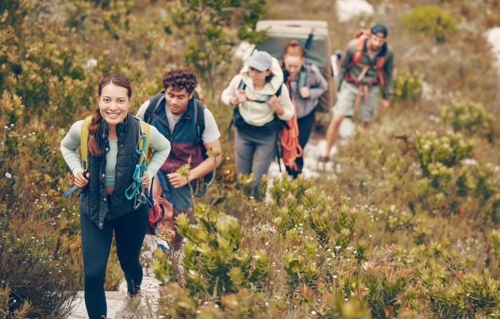Group of friends hike trail up mountain, to camp in nature landscape on extreme adventure holiday. Team of people explore earth together, on hiking trip to mountains or hill while on vacation.