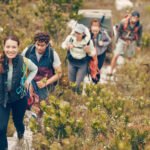 Group of friends hike trail up mountain, to camp in nature landscape on extreme adventure holiday. Team of people explore earth together, on hiking trip to mountains or hill while on vacation.