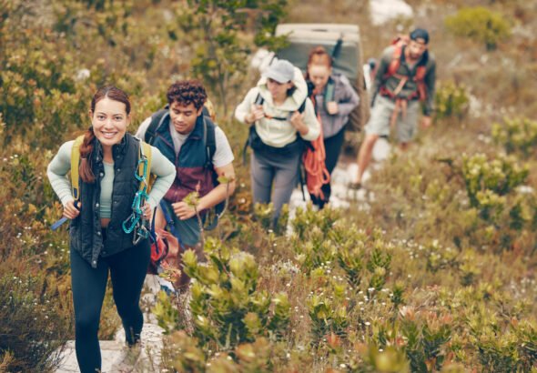 Group of friends hike trail up mountain, to camp in nature landscape on extreme adventure holiday. Team of people explore earth together, on hiking trip to mountains or hill while on vacation.