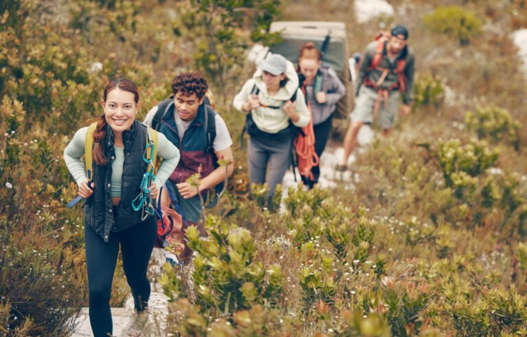 Group of friends hike trail up mountain, to camp in nature landscape on extreme adventure holiday. Team of people explore earth together, on hiking trip to mountains or hill while on vacation.
